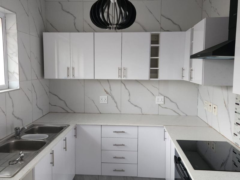 Modern kitchen featuring white cabinetry, marble-look wall tiles, stone countertops, integrated oven, and a sleek black extractor fan.