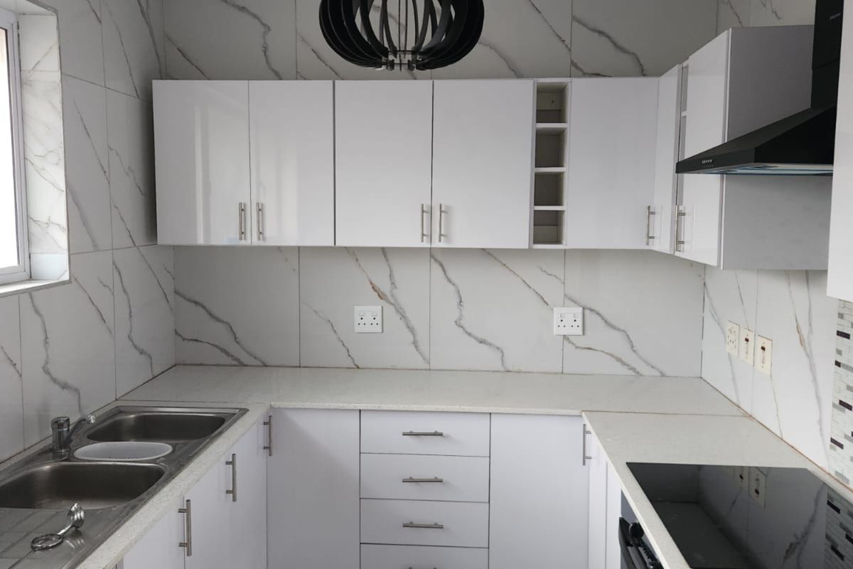 Modern kitchen featuring white cabinetry, marble-look wall tiles, stone countertops, integrated oven, and a sleek black extractor fan.