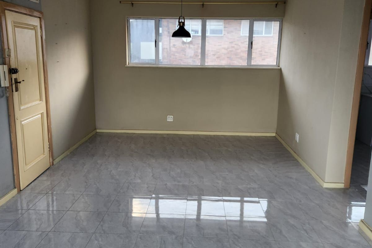 An empty living area featuring modern grey floor tiles, a ceiling-mounted light fixture, and a wall-mounted air conditioning unit.