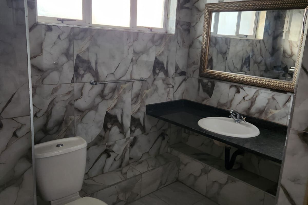 A bathroom featuring marble-effect wall tiling, a built-in vanity with a granite countertop, a ceramic basin, and a standard toilet.