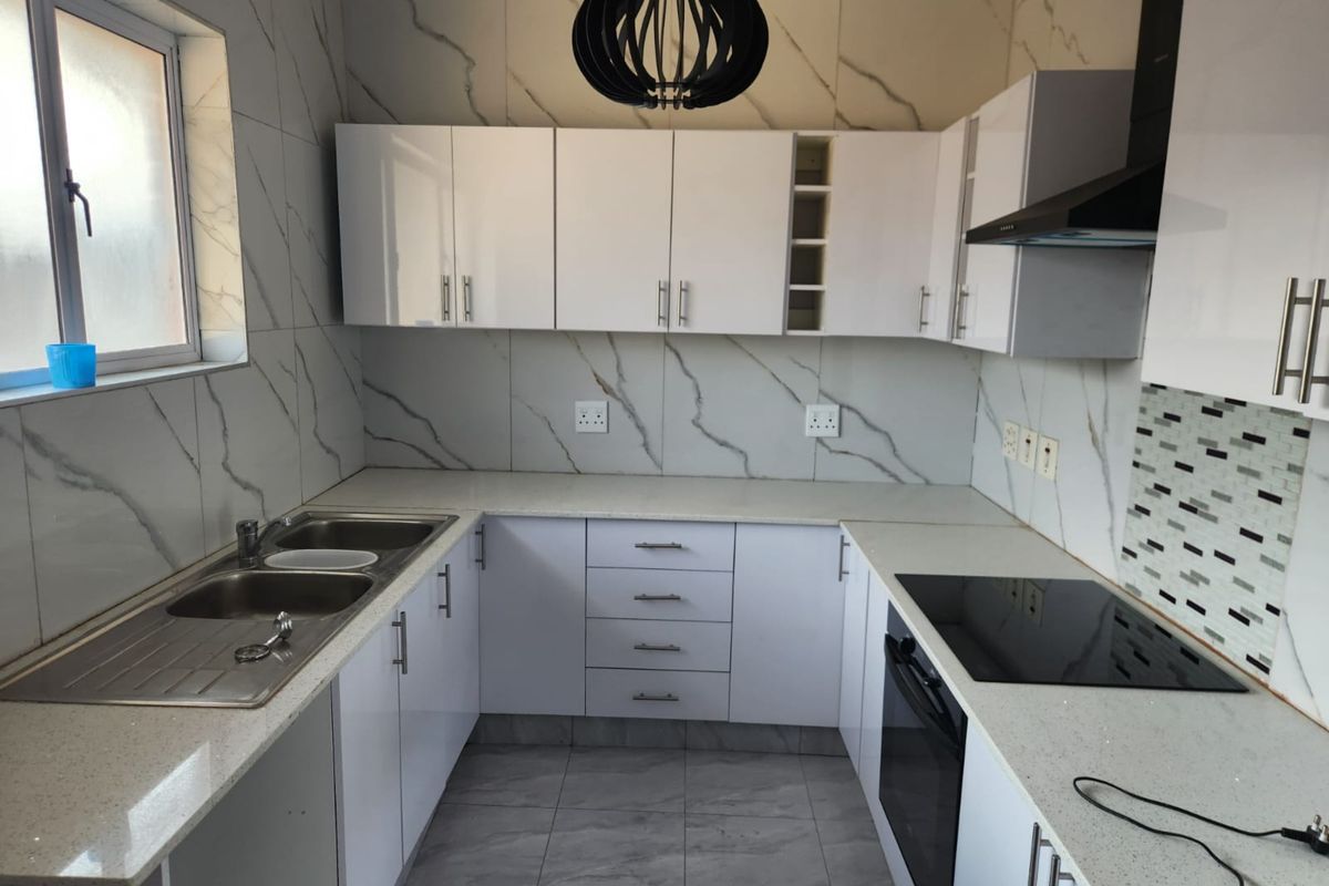 Modern kitchen featuring white high-gloss cabinetry, stone-look countertops, integrated electric hob, oven, extractor fan, and a double stainless steel sink.