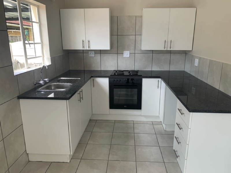 A clean, modern kitchen featuring white cabinetry, dark granite countertops, a built-in oven and hob, and neutral floor tiling.