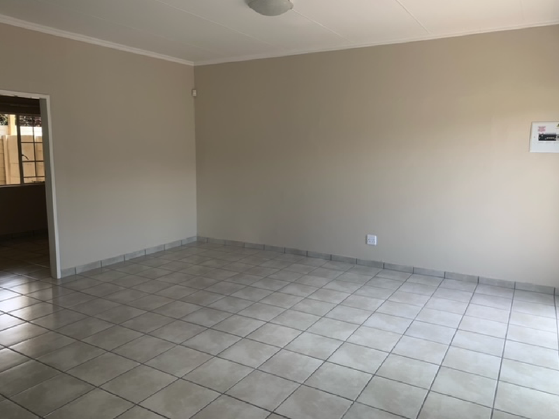 A spacious, empty living area featuring neutral tiled flooring, plain walls, and a ceiling-mounted light fixture.