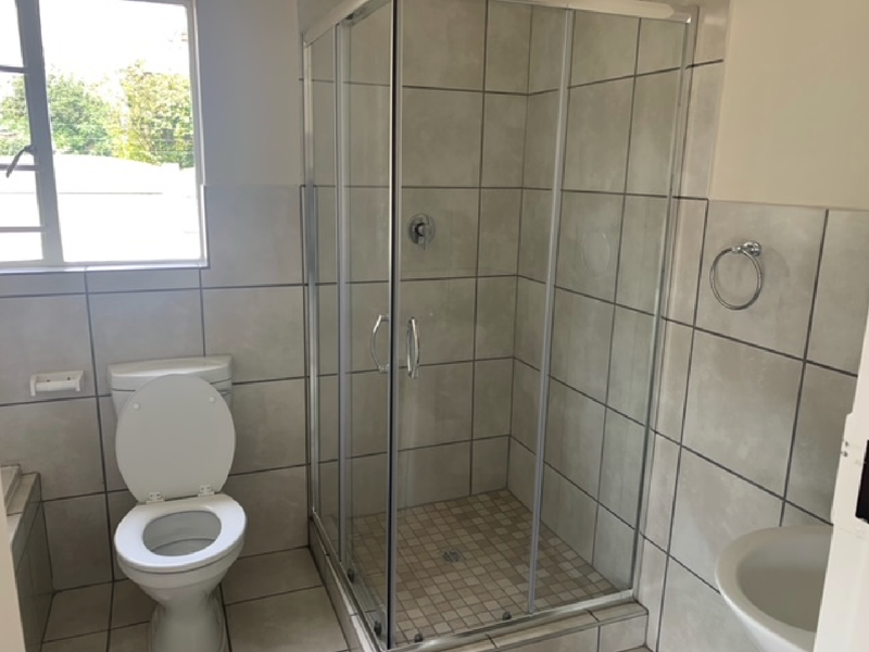 A functional bathroom featuring a glass-enclosed shower, a standard toilet, and tiled walls and flooring.