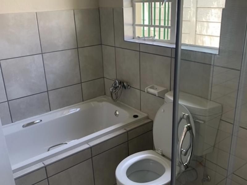A functional bathroom featuring a built-in bathtub with tiled surround, a standard toilet, and a glass-enclosed shower area with natural light.