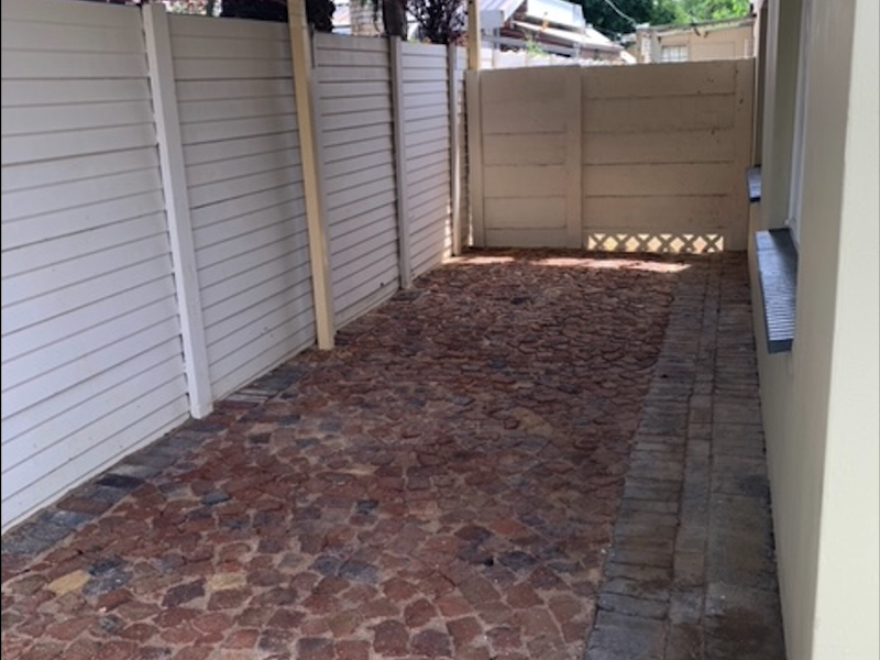 A covered outdoor patio area featuring rustic cobblestone paving and enclosed by white perimeter fencing.