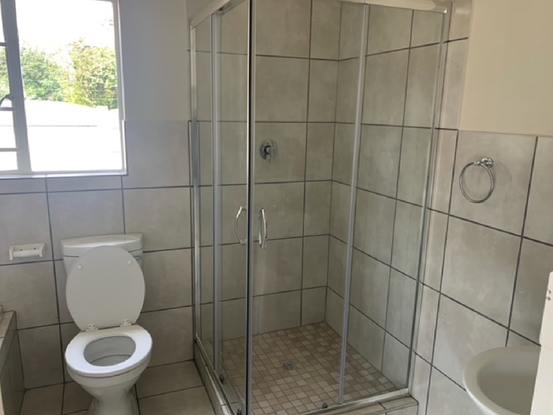 A functional bathroom featuring a glass-enclosed shower, a standard toilet, and tiled walls and flooring, providing a clean and practical space.
