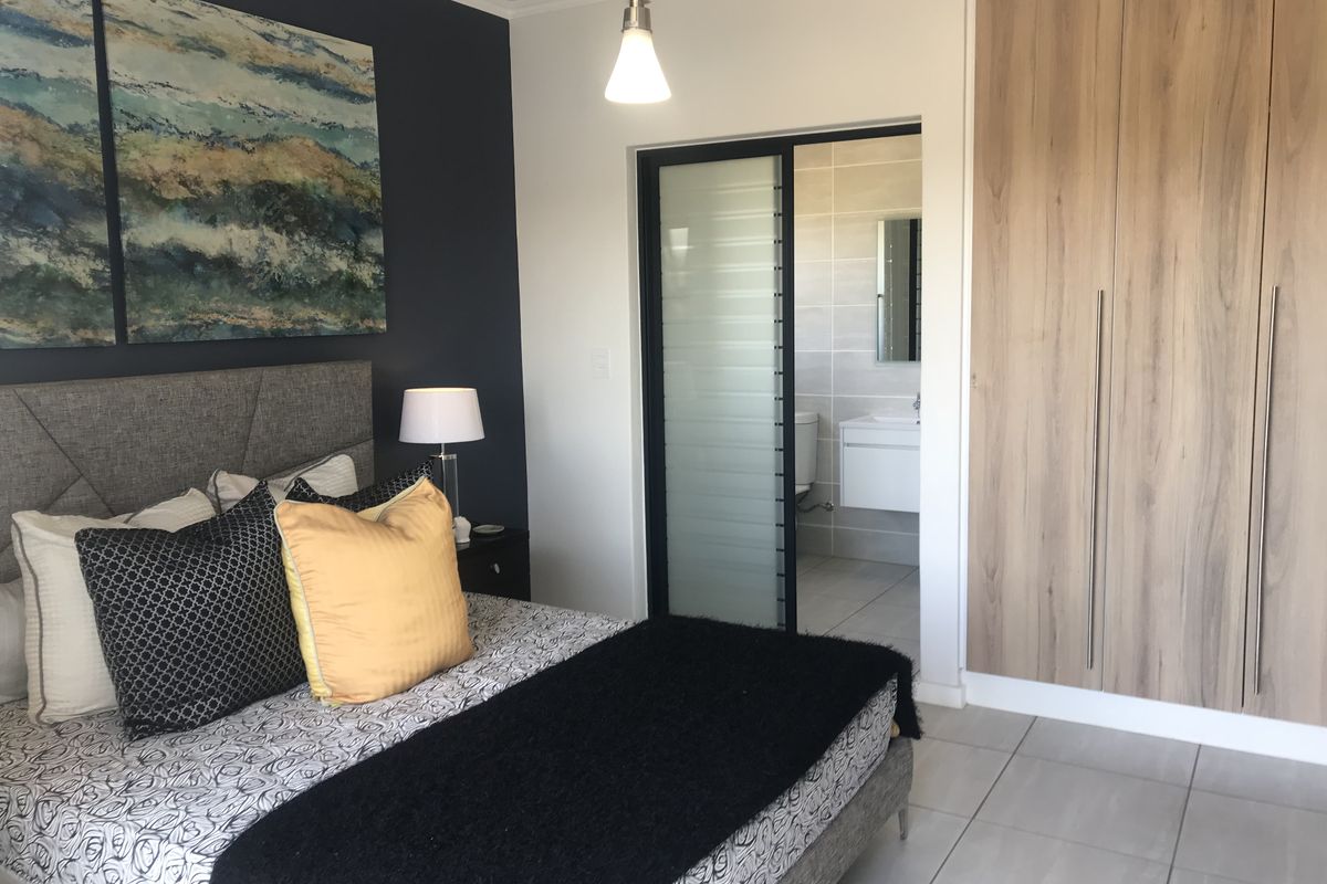 A modern bedroom featuring built-in wood-finish cupboards, tiled flooring, and an en-suite bathroom accessed via a sliding door.
