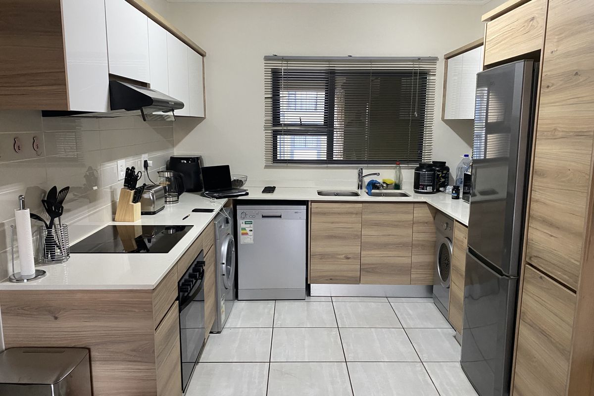 Modern kitchen featuring wood-grain cabinetry, white quartz countertops, integrated appliances, and tiled flooring with a functional layout.
