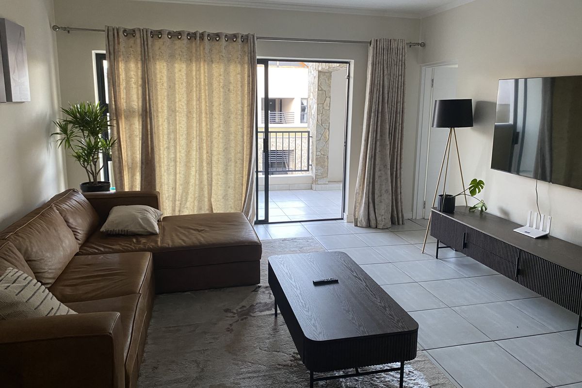 A well-maintained living room featuring neutral tiled flooring and a large sliding glass door providing access to an outdoor balcony area.