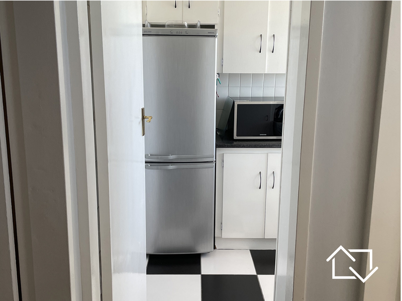 A compact kitchen featuring white cabinetry, a tiled backsplash, dark countertops, and a classic black and white checkered floor.