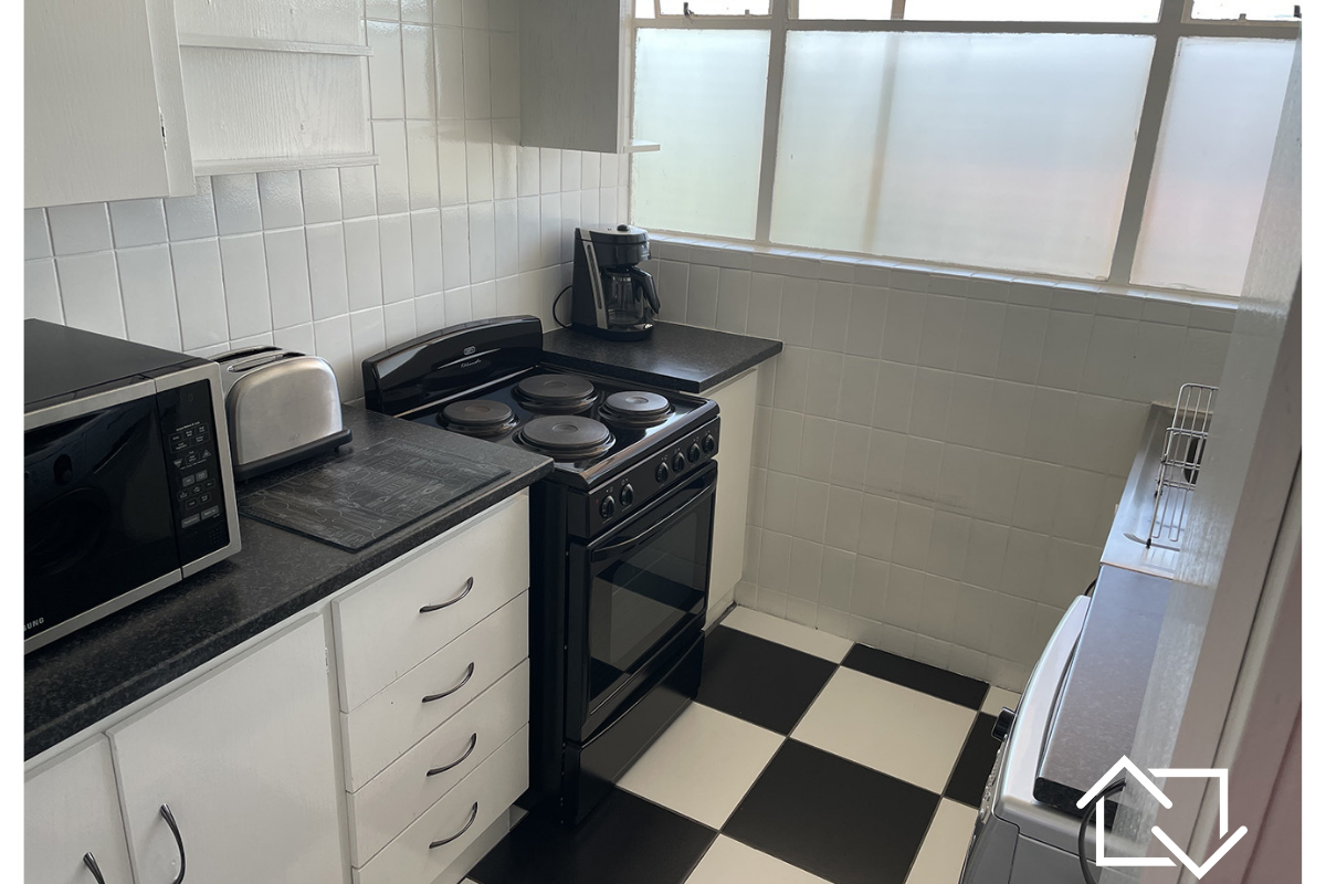 Compact kitchen featuring tiled splashbacks, laminate countertops, and a freestanding electric stove, with classic black and white checkered flooring.