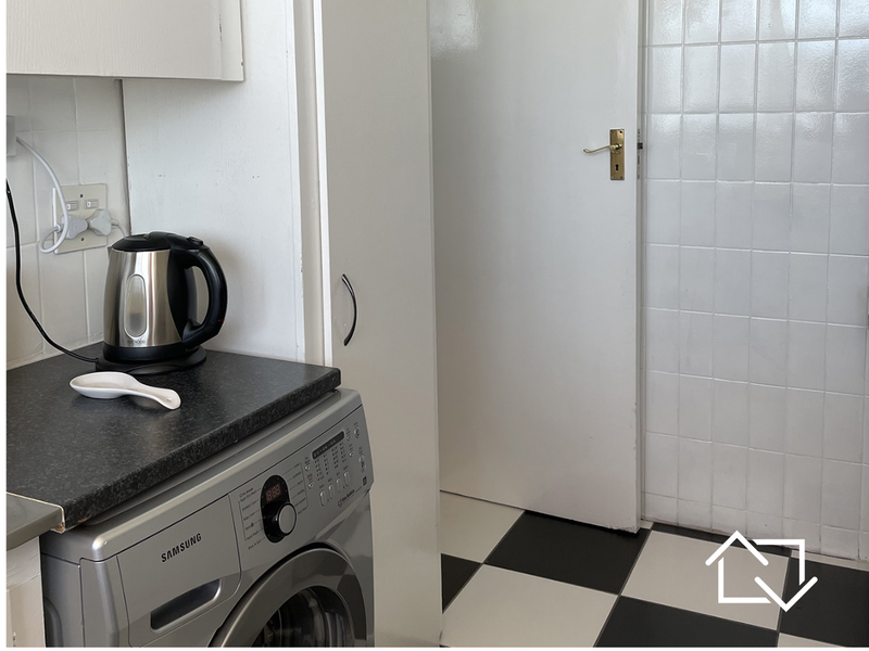 A functional laundry area featuring checkered floor tiles, tiled walls, and built-in cabinetry with a laminate countertop.