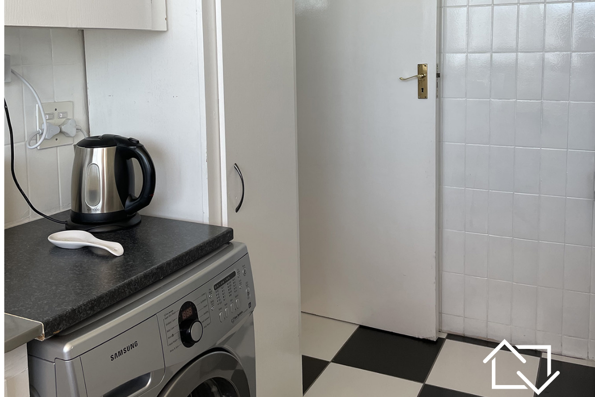 A functional laundry area featuring checkered floor tiles, tiled walls, and built-in cabinetry with a laminate countertop.