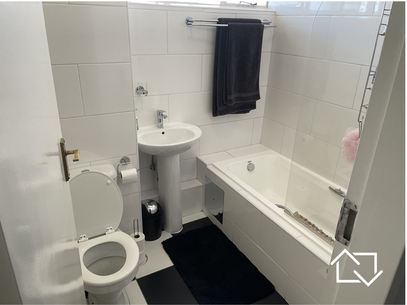 A clean, functional bathroom featuring a pedestal basin, toilet, and a bathtub with a glass shower screen, finished with white wall tiles.