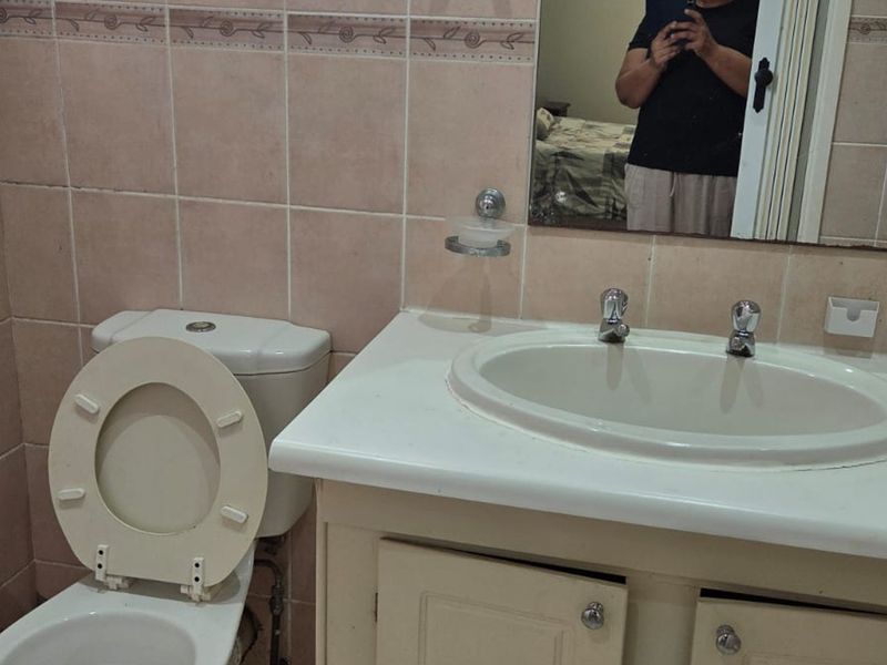 A dated bathroom featuring a vanity cabinet with a ceramic basin, wall-mounted mirror, and tiled walls.
