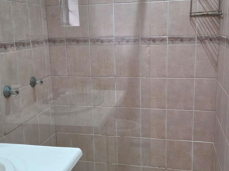 A functional bathroom featuring a tiled shower enclosure with a glass screen and a wall-mounted vanity basin with chrome fixtures.