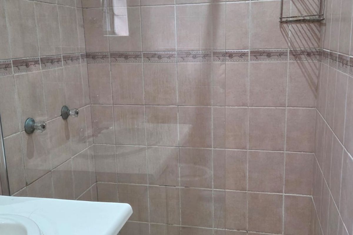 A functional bathroom featuring a tiled shower enclosure with a glass screen and a wall-mounted vanity basin with chrome fixtures.