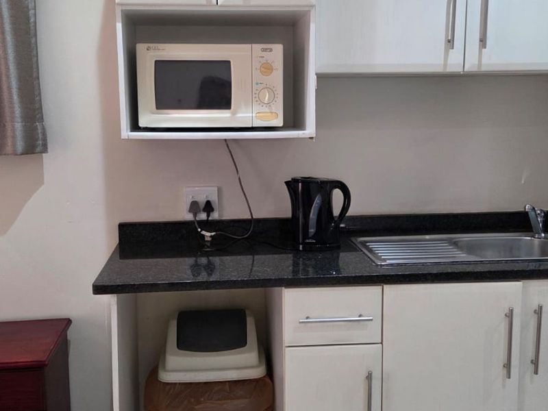 A compact kitchen area featuring white cabinetry, a dark granite countertop, and a built-in microwave shelf.