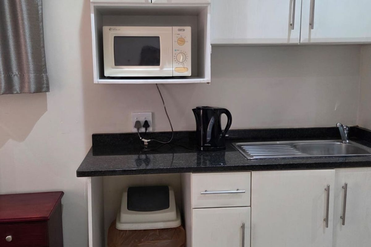 A compact kitchen area featuring white cabinetry, a dark granite countertop, and a built-in microwave shelf.