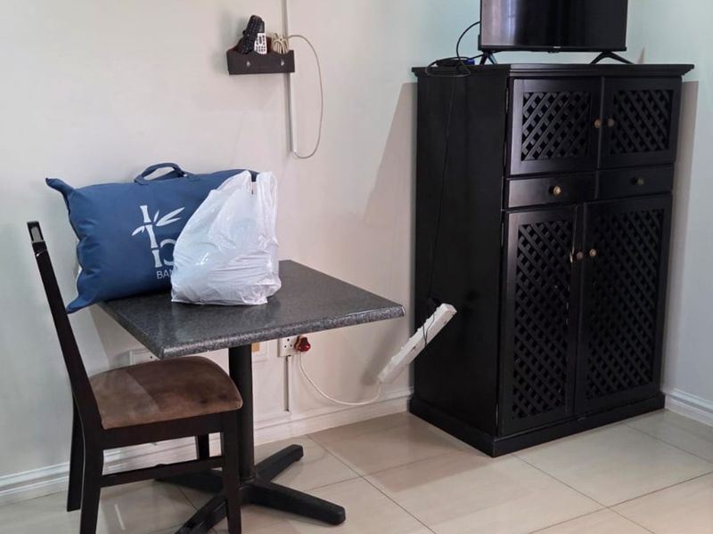 A bedroom corner featuring tiled flooring and neutral walls, currently utilized with a small dining table and storage cabinet.