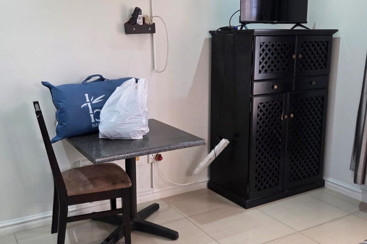 A bedroom corner featuring tiled flooring and neutral walls, currently utilized with a small dining table and storage cabinet.
