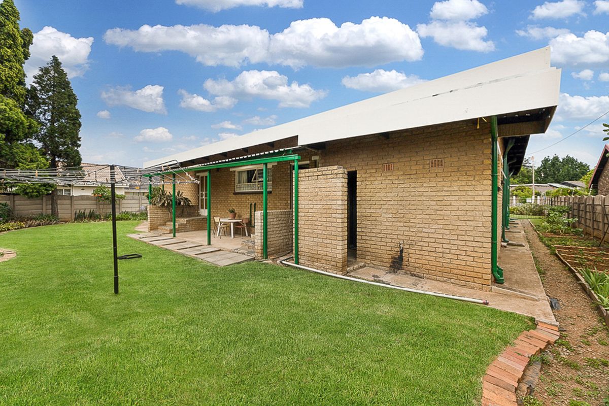 Rear view of the property featuring a brick facade, covered patio area, and a well-maintained lawn with established garden borders.