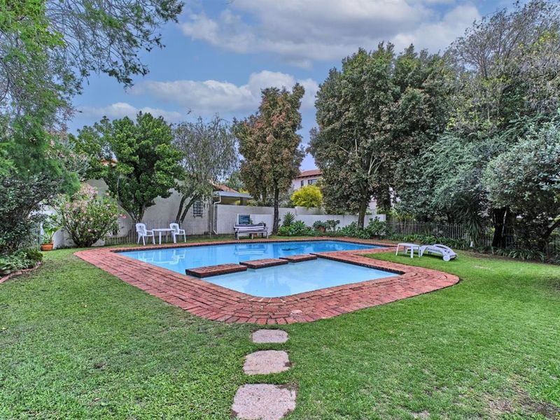 A private outdoor pool area featuring a swimming pool with brick coping, surrounded by a landscaped garden and mature trees.