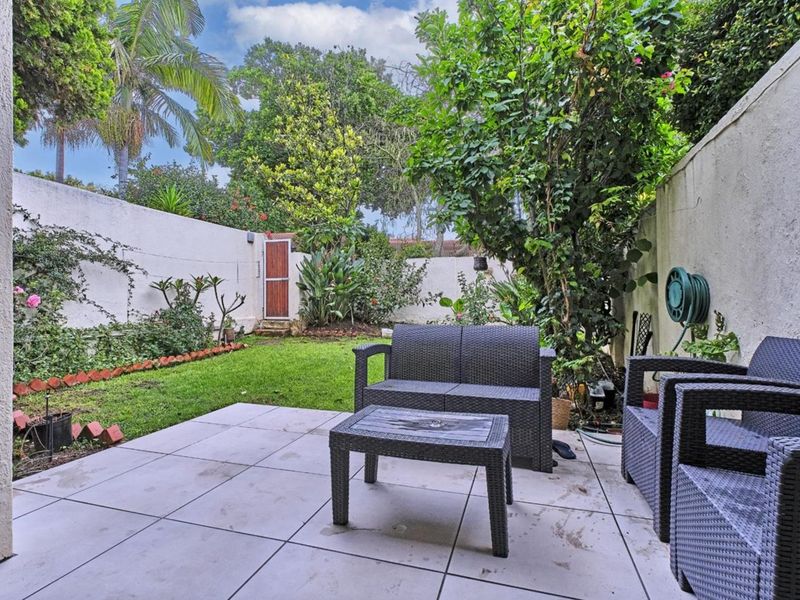 A private rear patio area featuring tiled flooring, a small lawn, and a secure boundary wall with a garden gate.