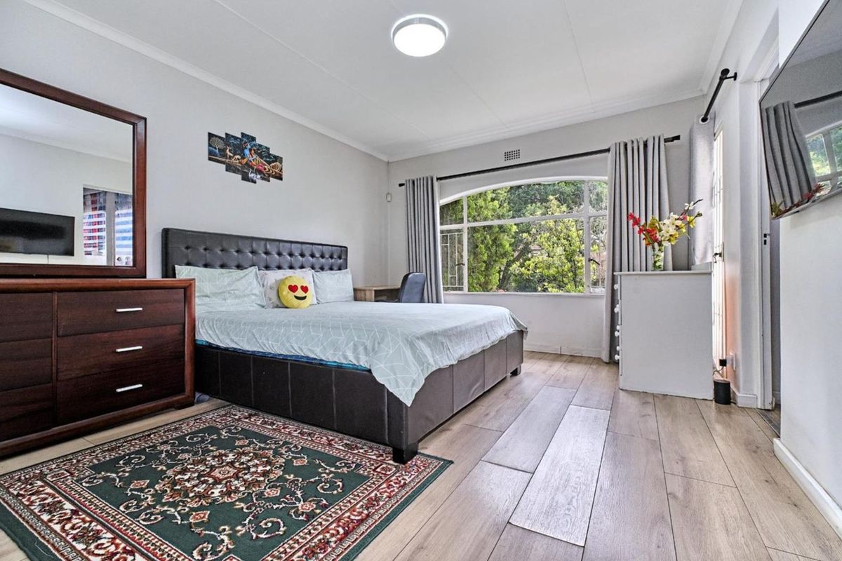 A well-lit bedroom featuring modern laminate flooring, neutral wall tones, and a large arched window providing natural light and garden views.