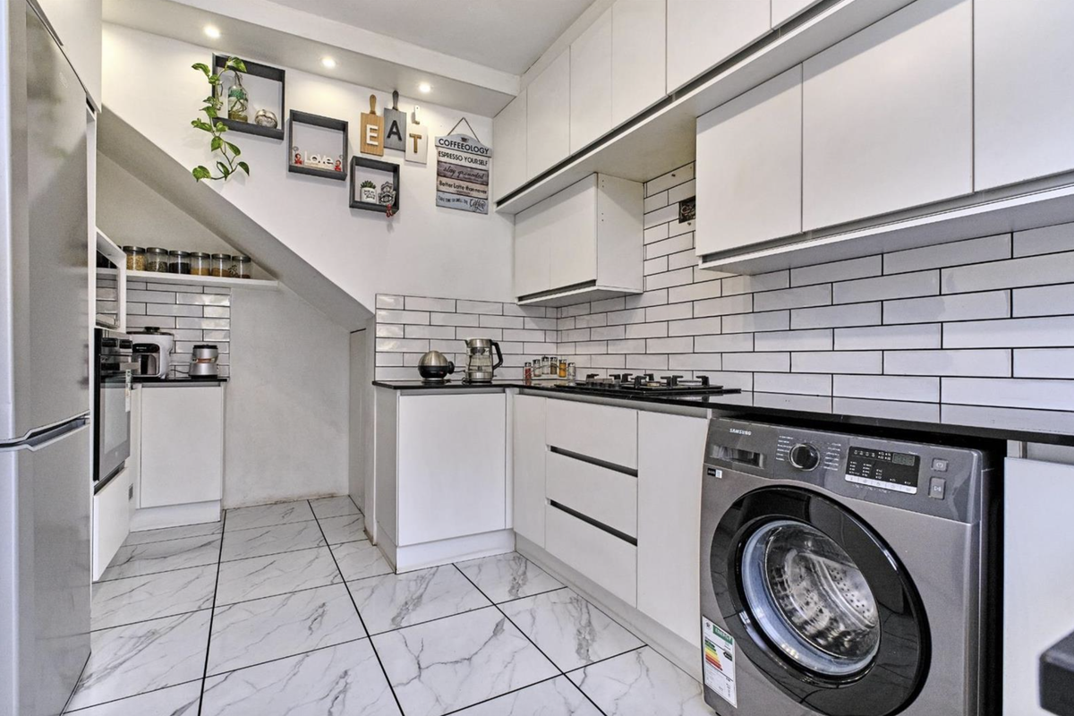 Modern kitchen featuring white cabinetry, subway tile backsplash, stone countertops, and integrated appliances, with a unique layout tucked under the staircase.