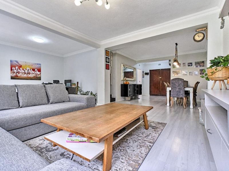 Spacious open-plan living and dining area featuring light-toned laminate flooring, crown molding, and a seamless flow between the lounge and dining space.
