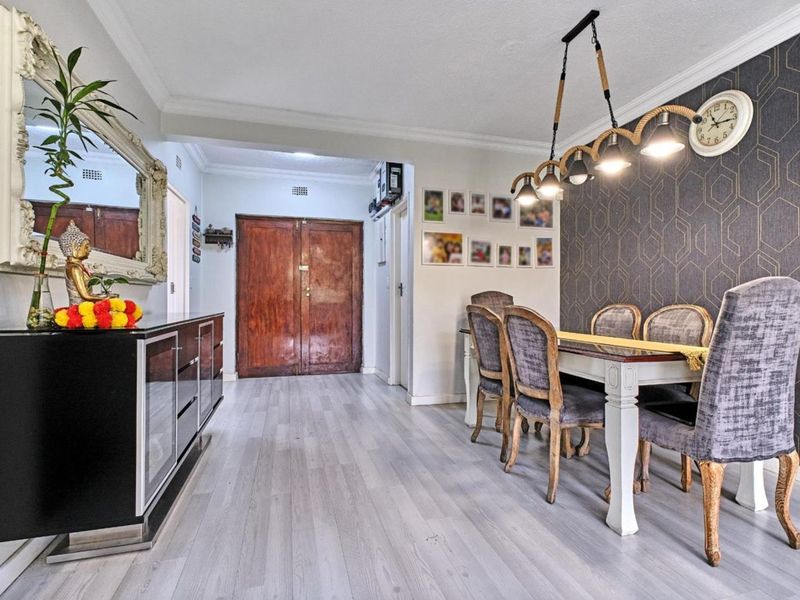 A well-maintained dining area featuring modern laminate flooring, a striking geometric feature wall, and stylish pendant lighting.