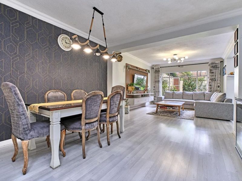 Spacious open-plan living and dining area featuring modern laminate flooring, a striking feature wall, and a built-in media unit with access to the garden.