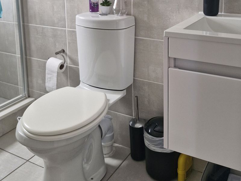 A modern bathroom featuring a white toilet, a wall-mounted vanity cabinet with an integrated sink, and neutral-toned wall and floor tiles.