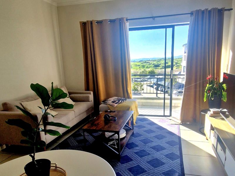 A bright living room featuring tiled flooring and a large sliding glass door that opens onto a balcony with scenic outdoor views.
