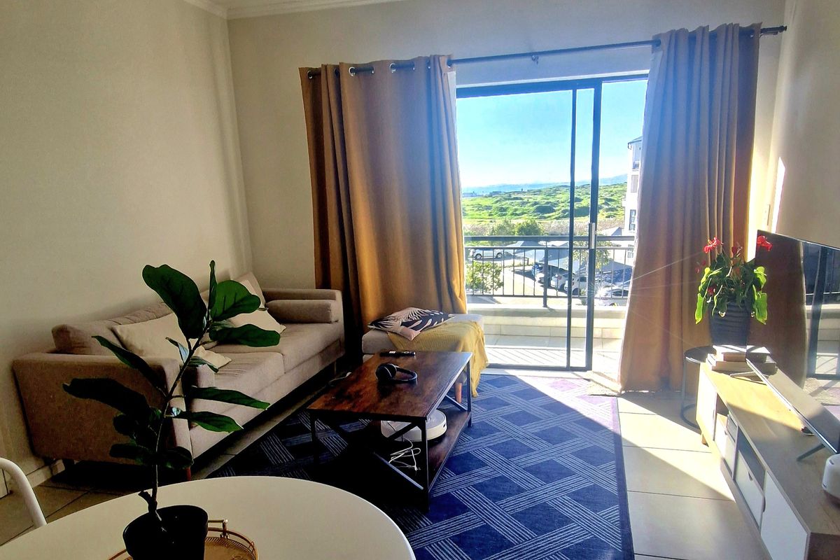 A bright living room featuring tiled flooring and a large sliding glass door that opens onto a balcony with scenic outdoor views.