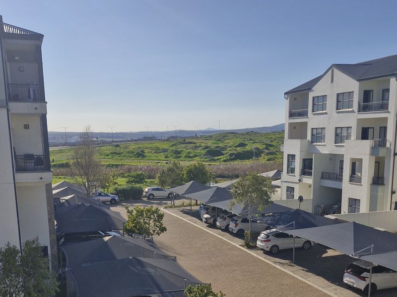 View of the apartment complex exterior, featuring paved parking areas with shade cloth carports and multi-story residential building facades.