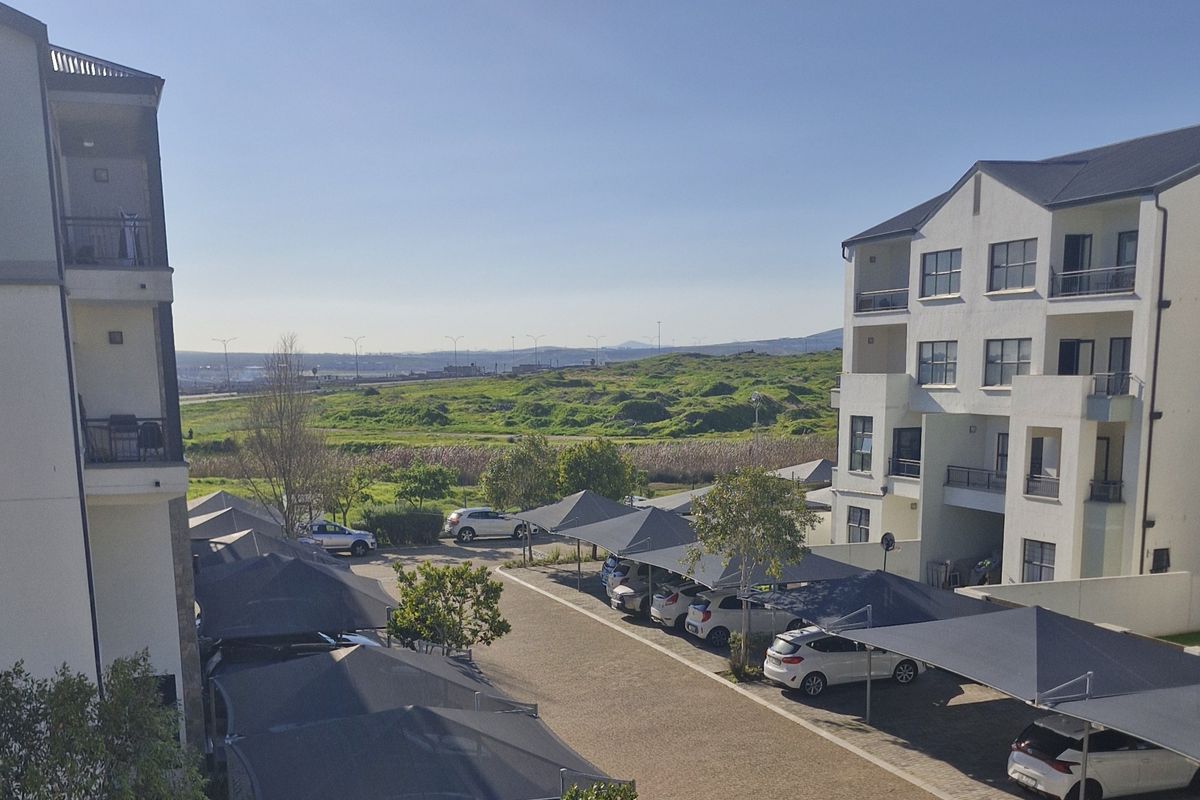 View of the apartment complex exterior, featuring paved parking areas with shade cloth carports and multi-story residential building facades.