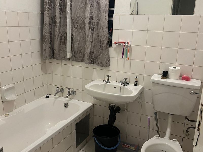 A functional bathroom featuring a built-in bathtub, pedestal sink, and flush toilet, finished with white ceramic wall and floor tiles.