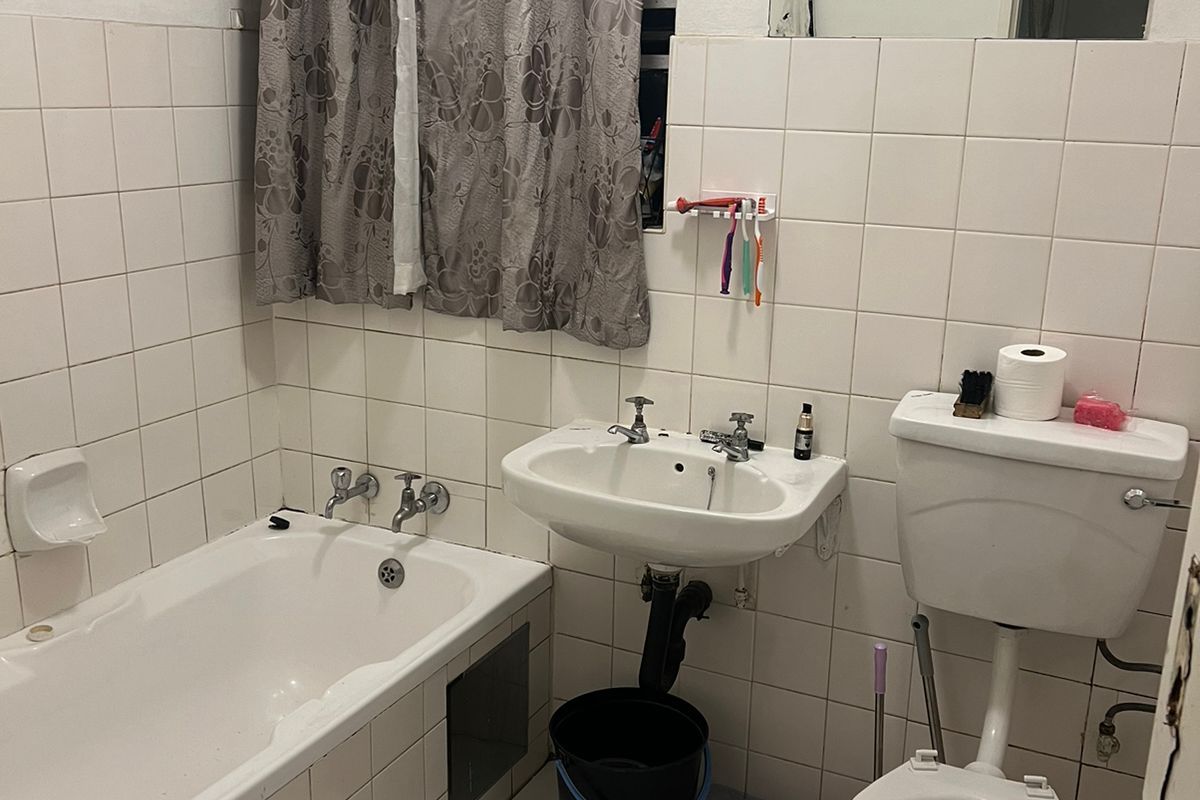 A functional bathroom featuring a built-in bathtub, pedestal sink, and flush toilet, finished with white ceramic wall and floor tiles.