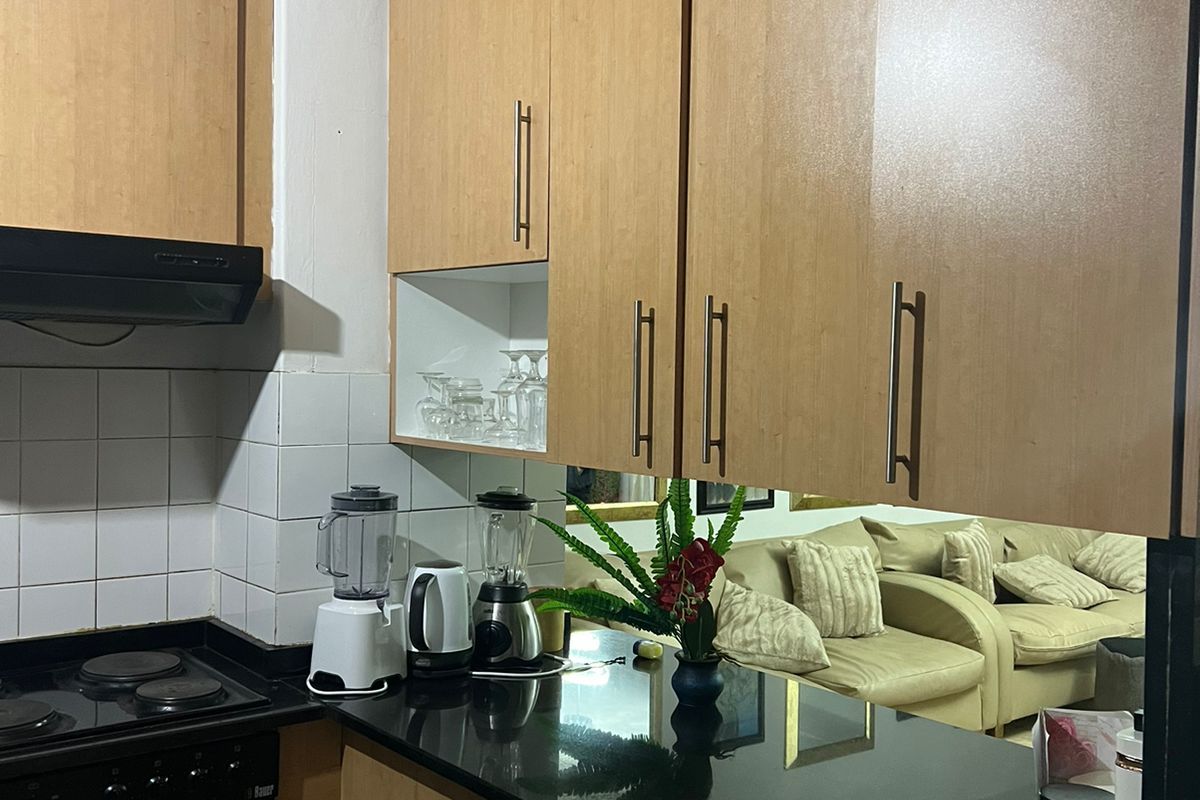 A functional kitchen featuring light wood-finish cabinetry, black granite countertops, a built-in oven, and an electric hob with an integrated extractor fan.