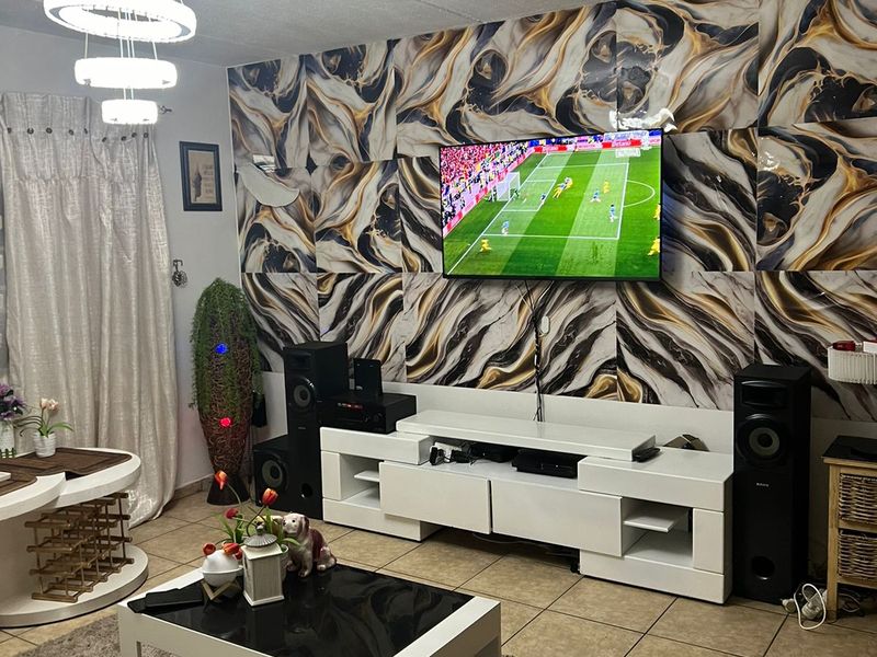 A living room featuring tiled flooring, a modern pendant light, and a bold patterned feature wall with a mounted television.