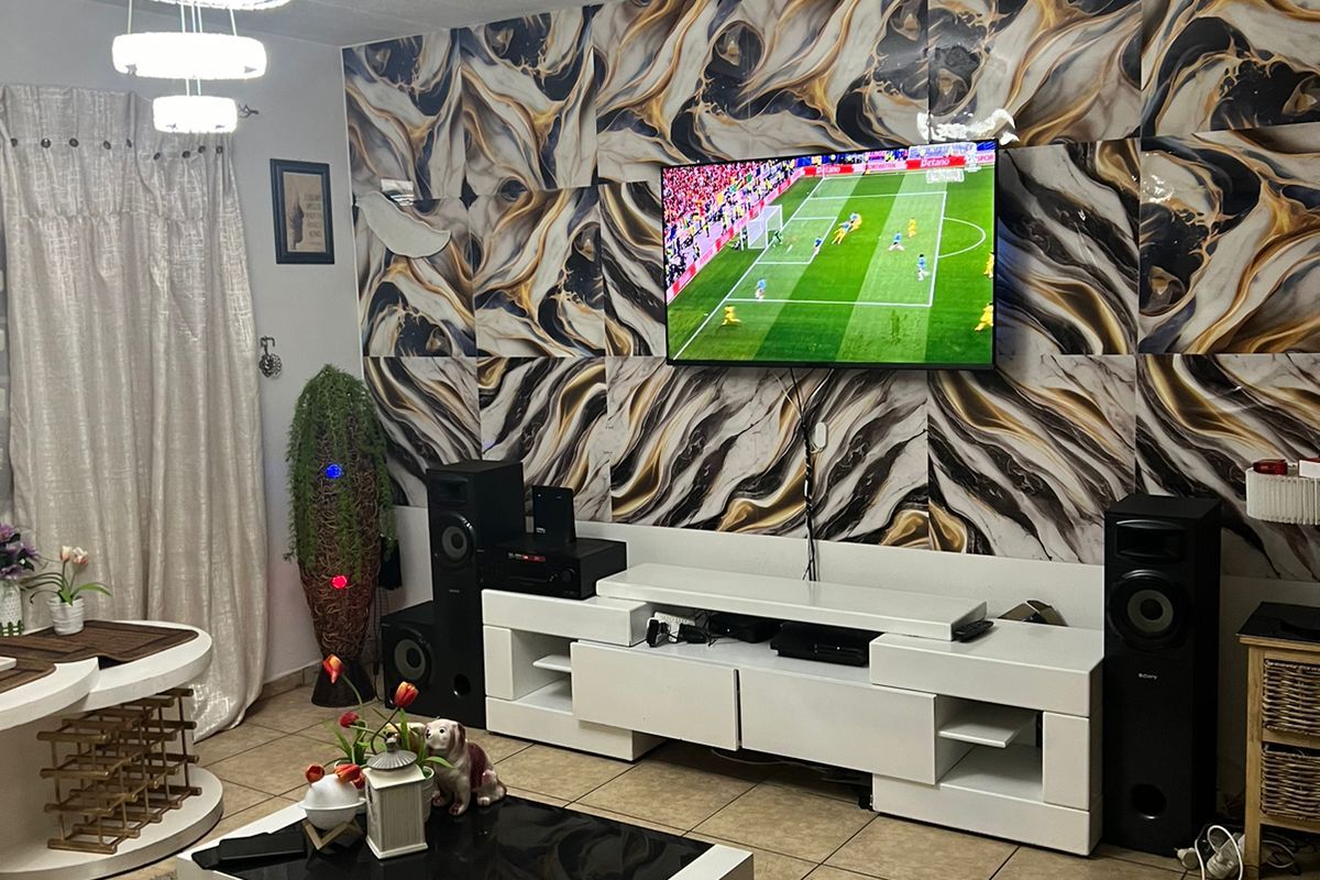 A living room featuring tiled flooring, a modern pendant light, and a bold patterned feature wall with a mounted television.