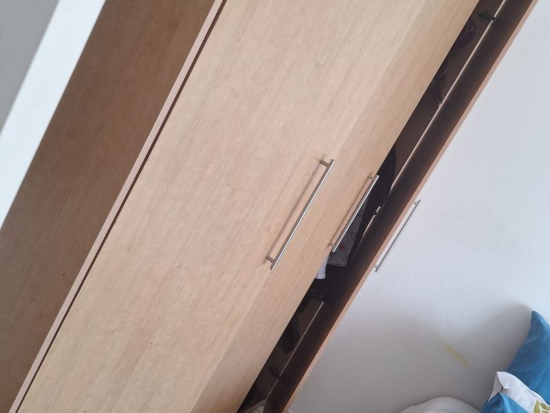 A bedroom featuring a light wood-finish built-in wardrobe and tiled flooring, with visible wall staining near the bed area.