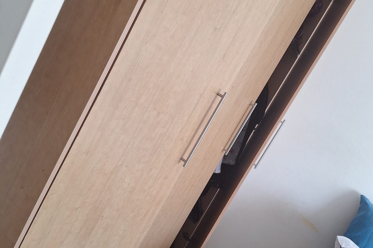 A bedroom featuring a light wood-finish built-in wardrobe and tiled flooring, with visible wall staining near the bed area.