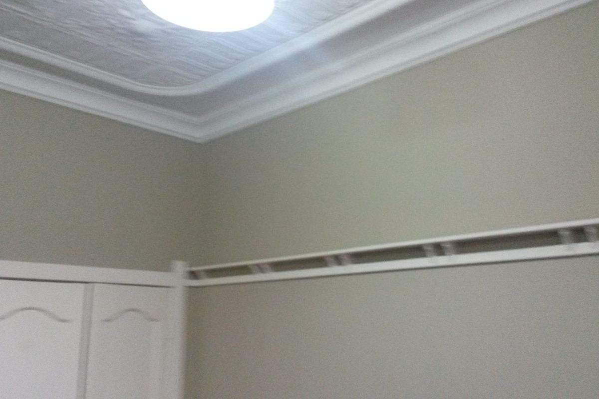 A bedroom interior featuring a built-in wardrobe, decorative ceiling cornice, and a traditional picture rail.