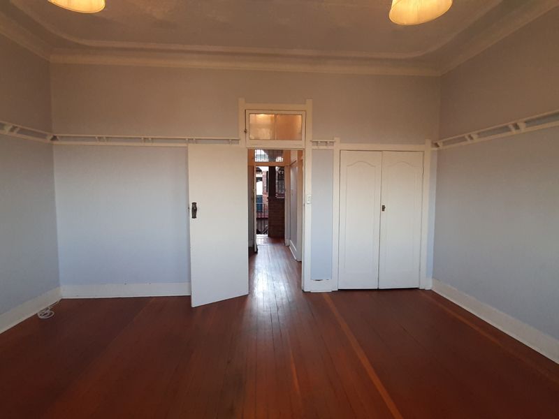 An empty bedroom featuring original timber flooring, picture rails, and a built-in wardrobe, offering a blank canvas for interior design.