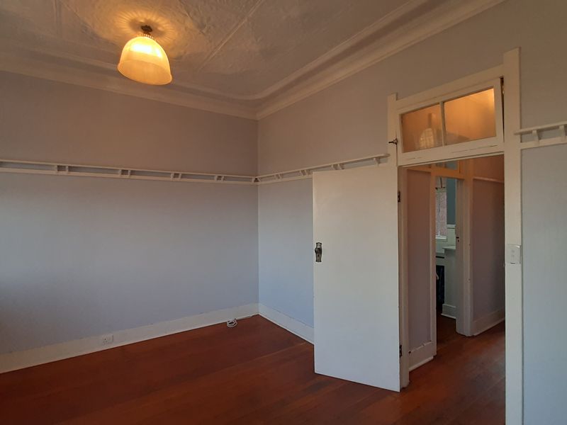 An empty bedroom featuring original timber flooring, decorative ceiling rose, picture rails, and a classic transom window above the doorway.