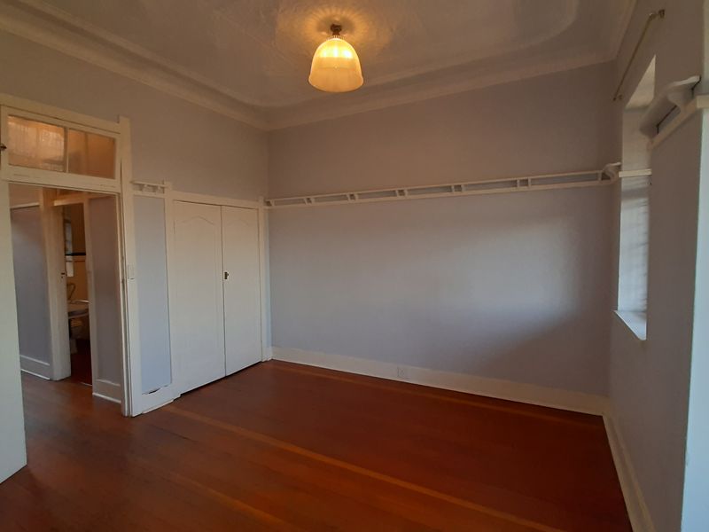 A bright, empty bedroom featuring original hardwood flooring, a built-in wardrobe, decorative ceiling rose, and classic picture rails.